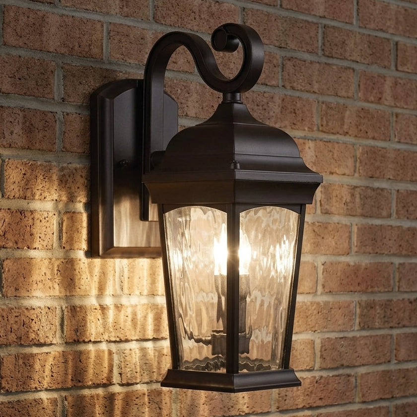Bronze S-arm wall lantern illuminated against brick