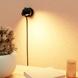 Wall-mounted lamp casting a warm glow on a book and plant in a cozy room.
