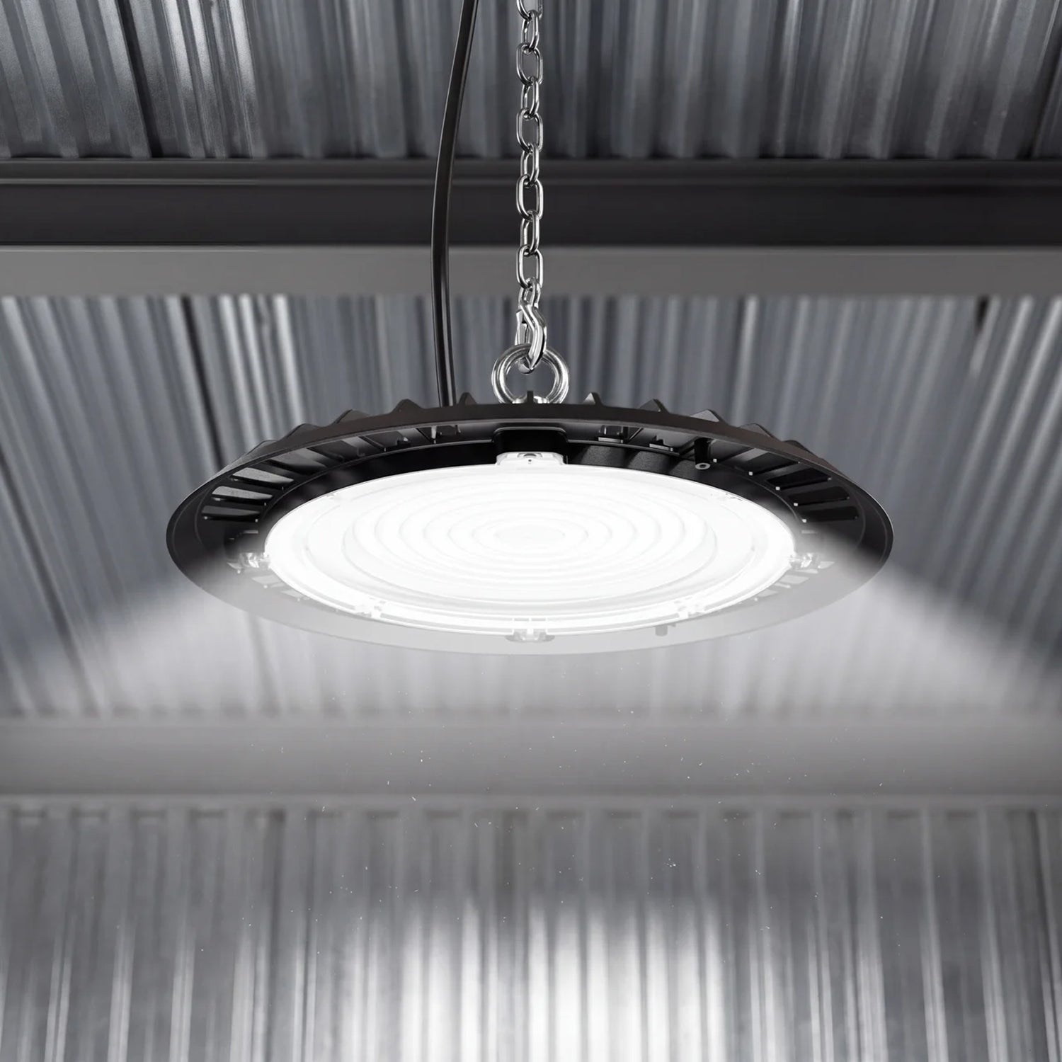 Lit UFO high bay suspended by chain under a corrugated metal ceiling, casting bright even light below.