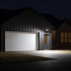 White two-head LED security floodlight with motion sensor lighting a driveway and garage door at night