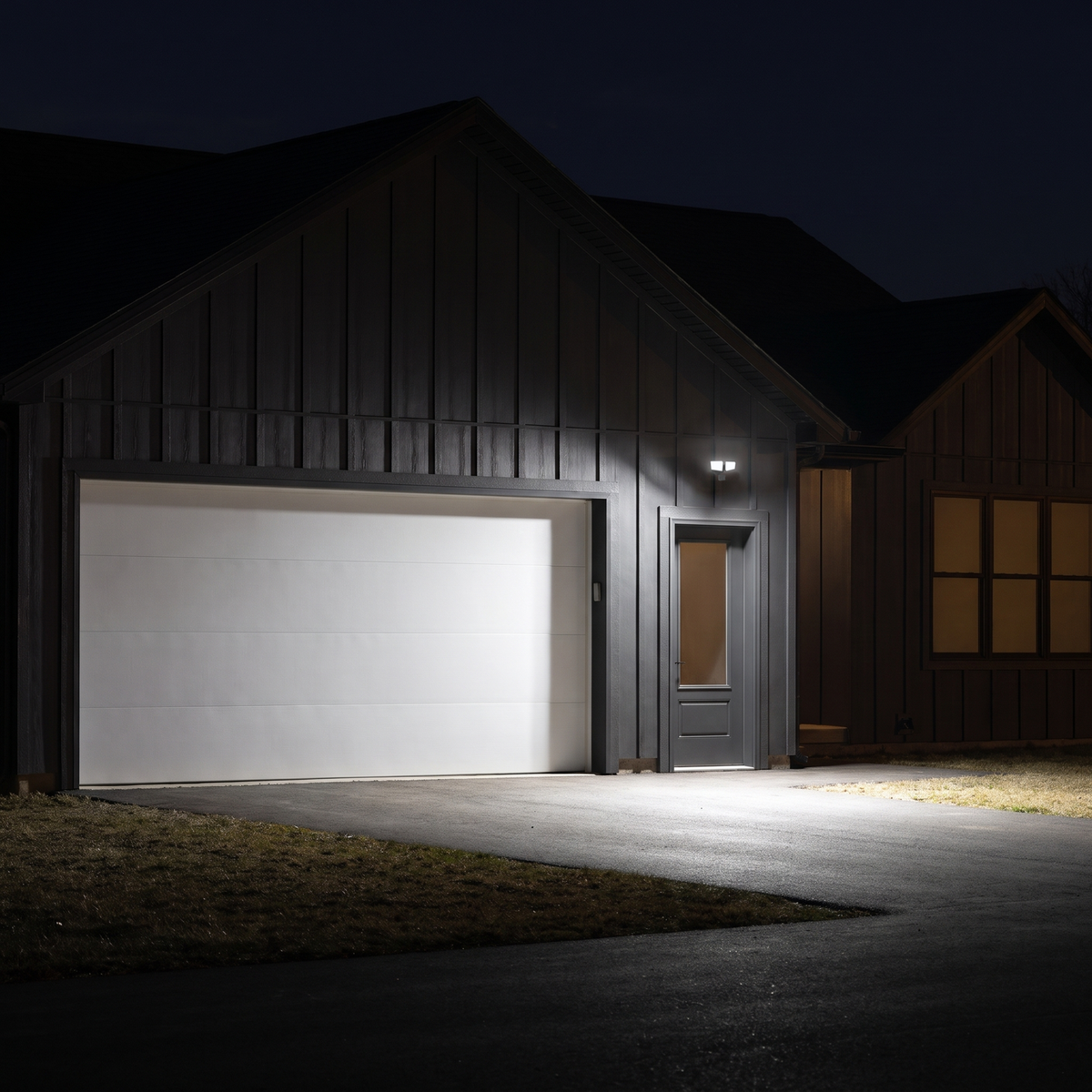 White two-head LED security floodlight with motion sensor lighting a driveway and garage door at night